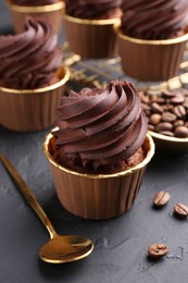 Photo of Delicious chocolate cupcakes and coffee beans on black textured table