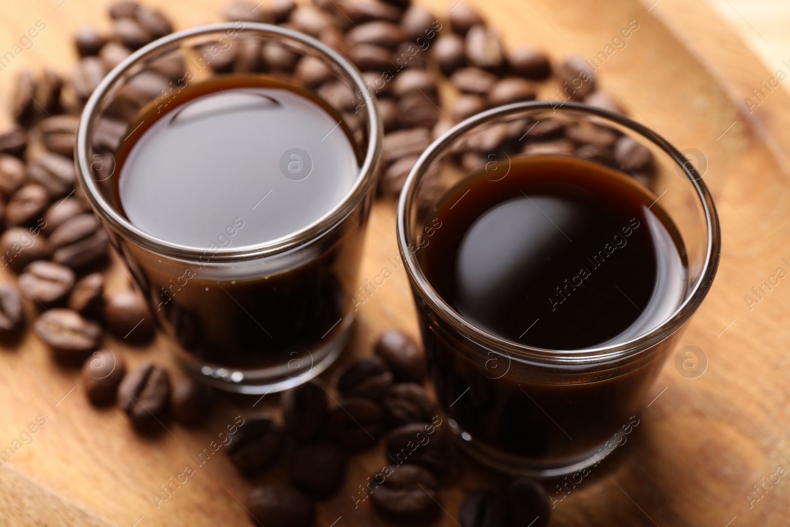 Photo of Shot glasses with coffee liqueur and beans on wooden tray, closeup