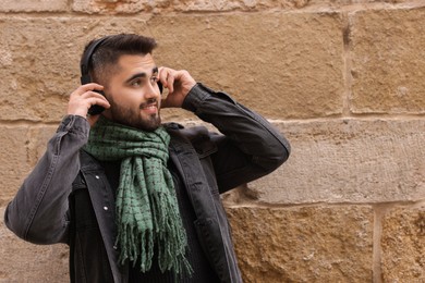 Photo of Smiling man in warm scarf listening to music near brick wall. Space for text