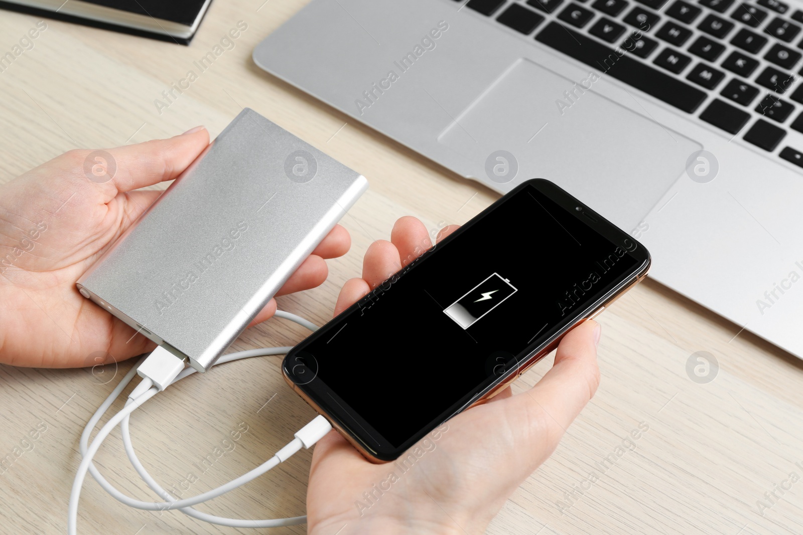 Photo of Woman charging mobile phone with power bank at wooden table, closeup