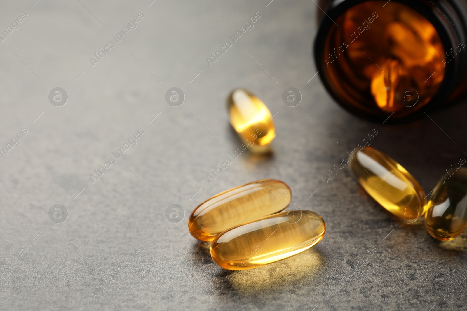 Photo of Dietary supplement capsules on grey table, closeup. Space for text