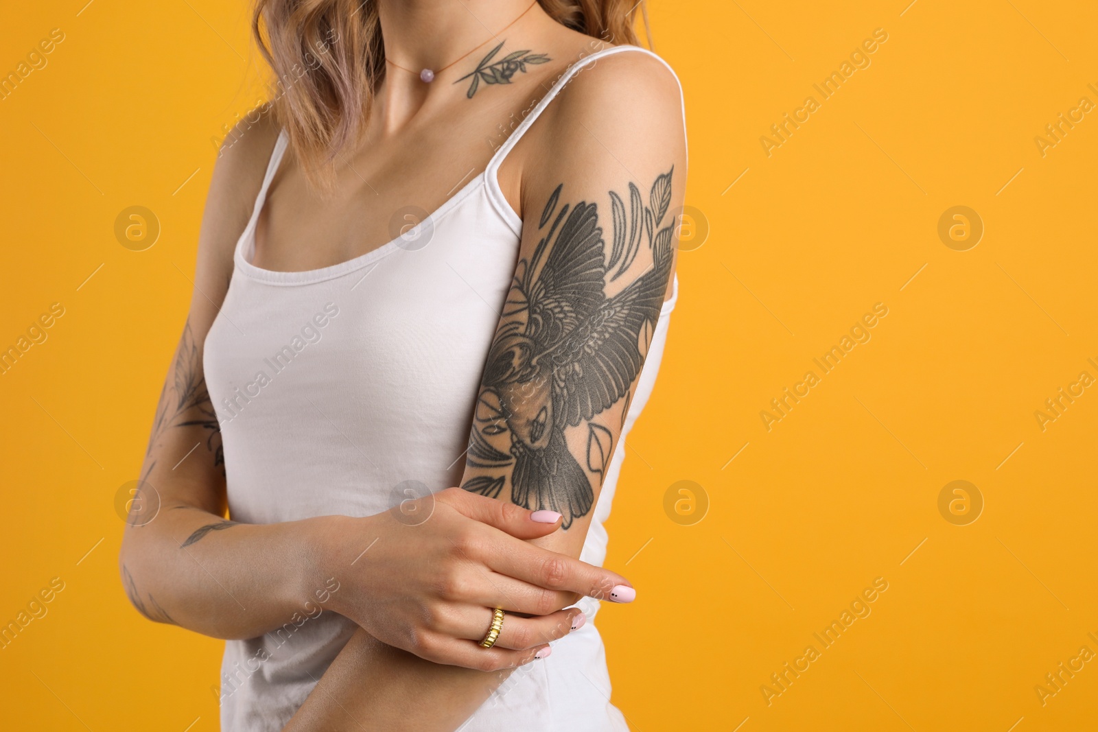 Photo of Beautiful woman with tattoos on body against yellow background, closeup. Space for text