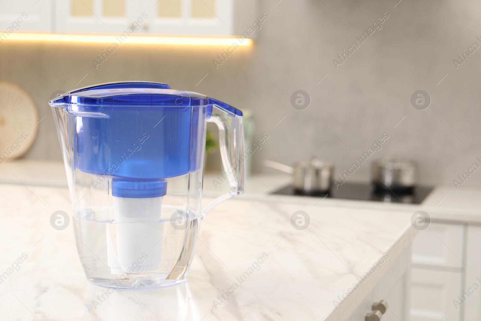 Photo of Water filter jug on white marble table in kitchen, space for text