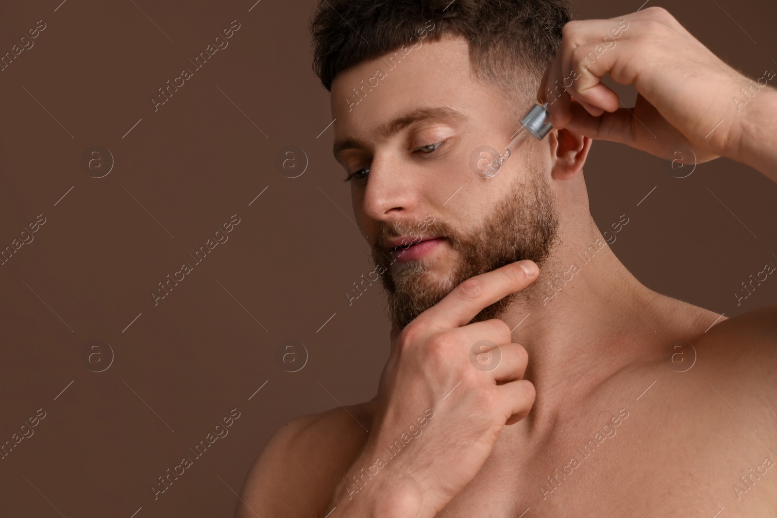 Photo of Handsome man applying serum onto his face on brown background, space for text