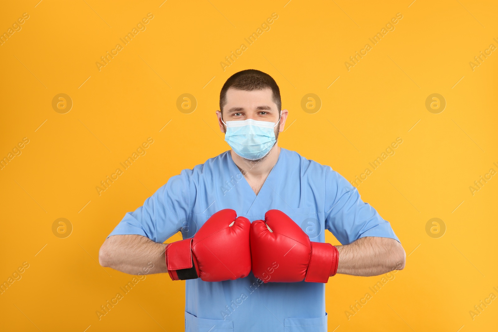 Photo of Doctor with protective mask and boxing gloves on yellow background. Strong immunity concept