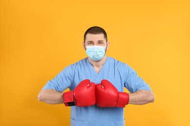 Doctor with protective mask and boxing gloves on yellow background. Strong immunity concept