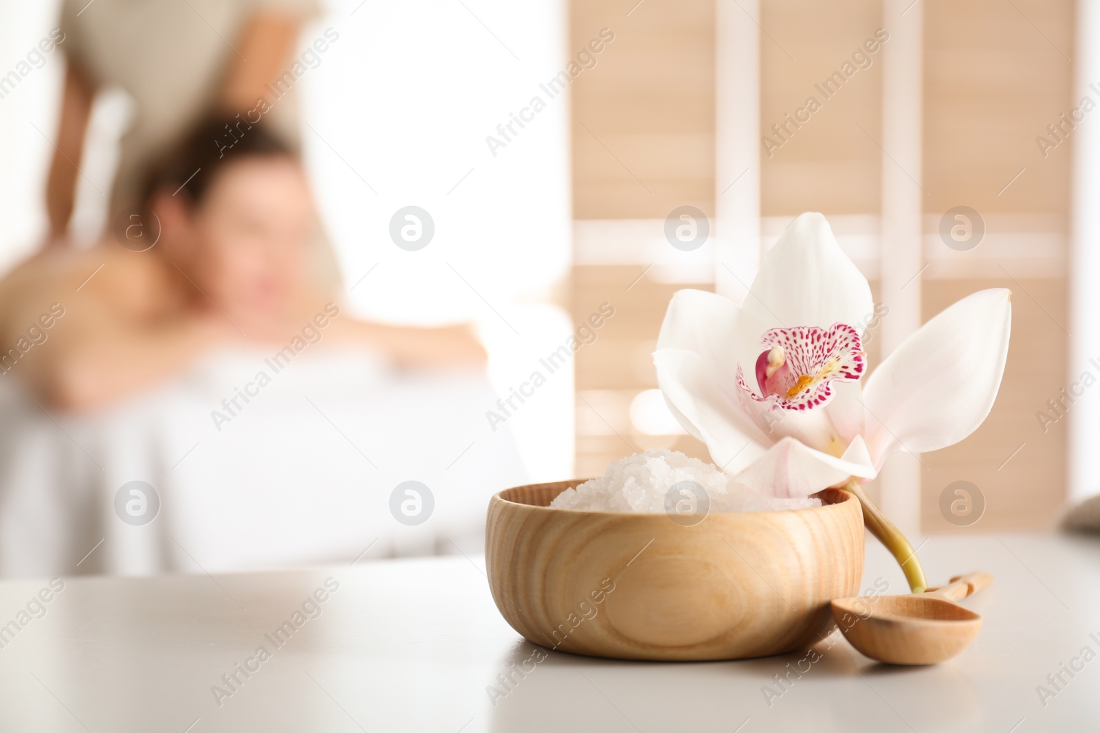 Photo of Bowl with sea salt and orchid flower on white table in spa salon. Space for text