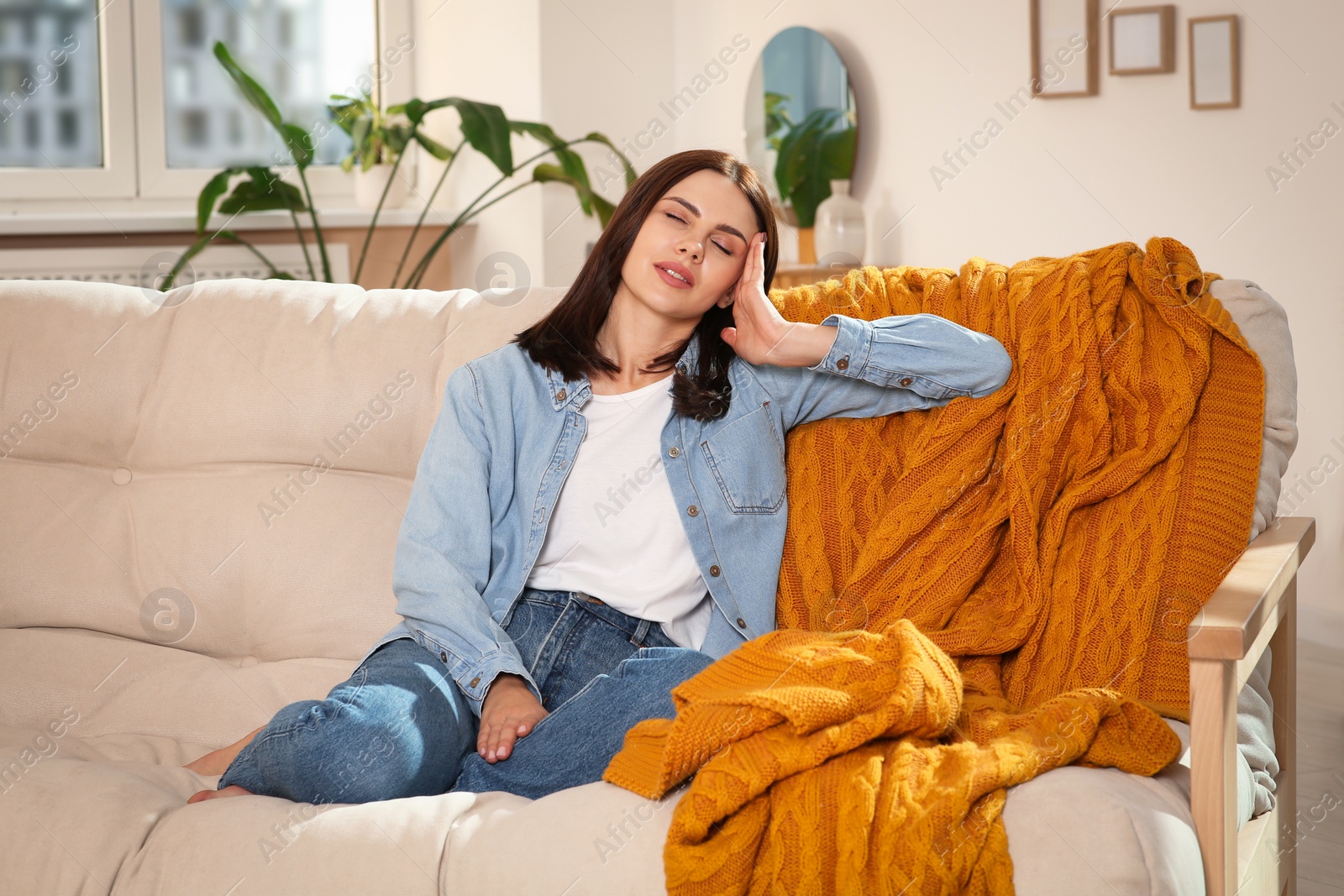 Photo of Young woman suffering from headache on sofa at home. Hormonal disorders