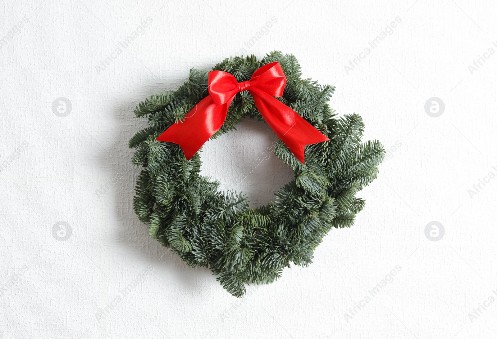 Photo of Christmas wreath made of fir tree branches with red ribbon on white textured background