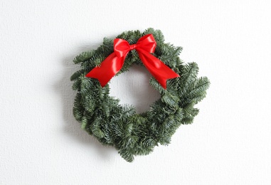 Photo of Christmas wreath made of fir tree branches with red ribbon on white textured background