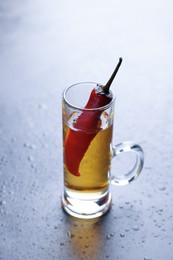 Photo of Red hot chili peppers and vodka in shot glass on grey table