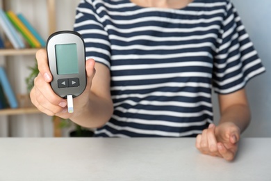 Photo of Woman holding glucometer at table. Diabetes test