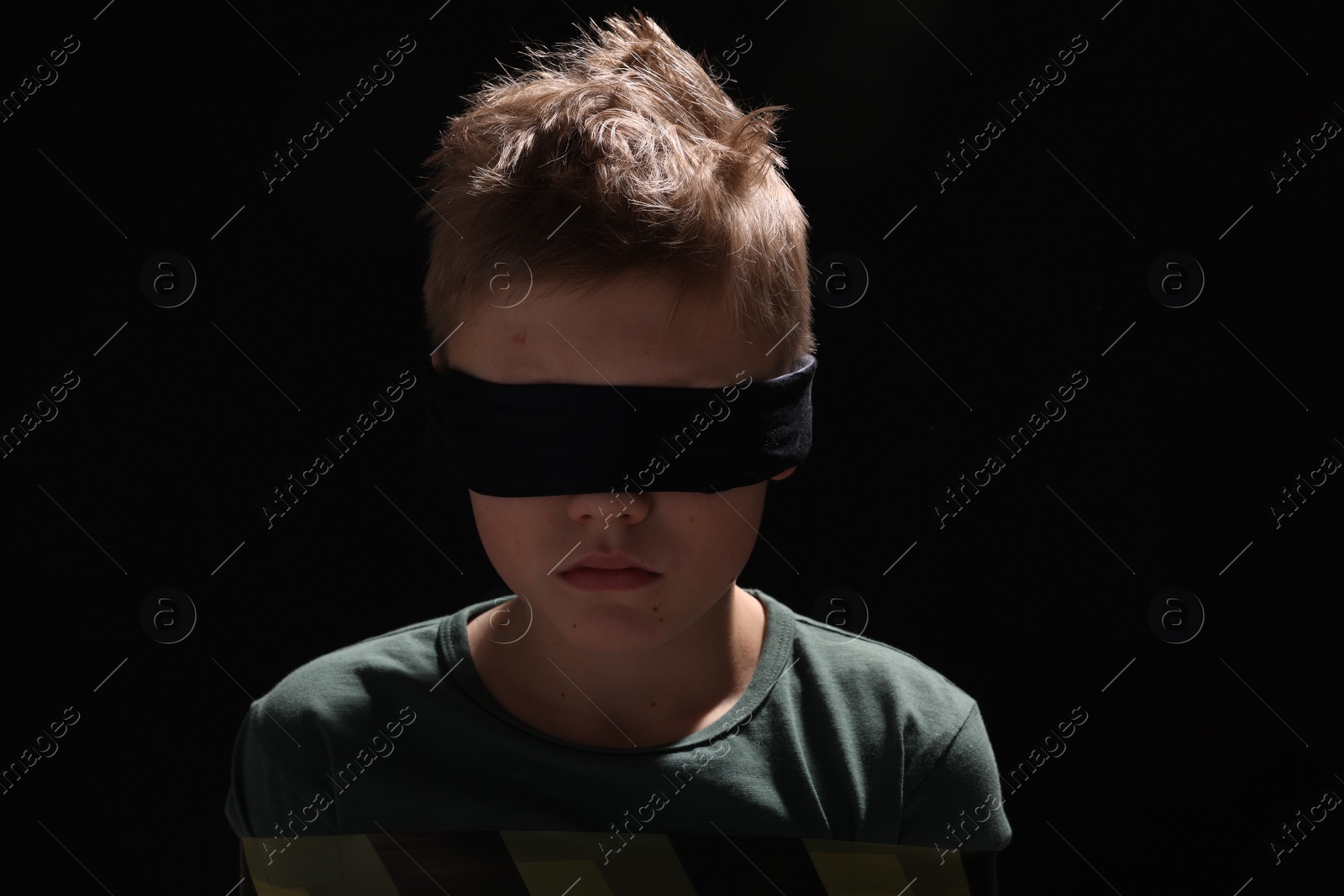 Photo of Blindfolded little boy tied up and taken hostage against dark background
