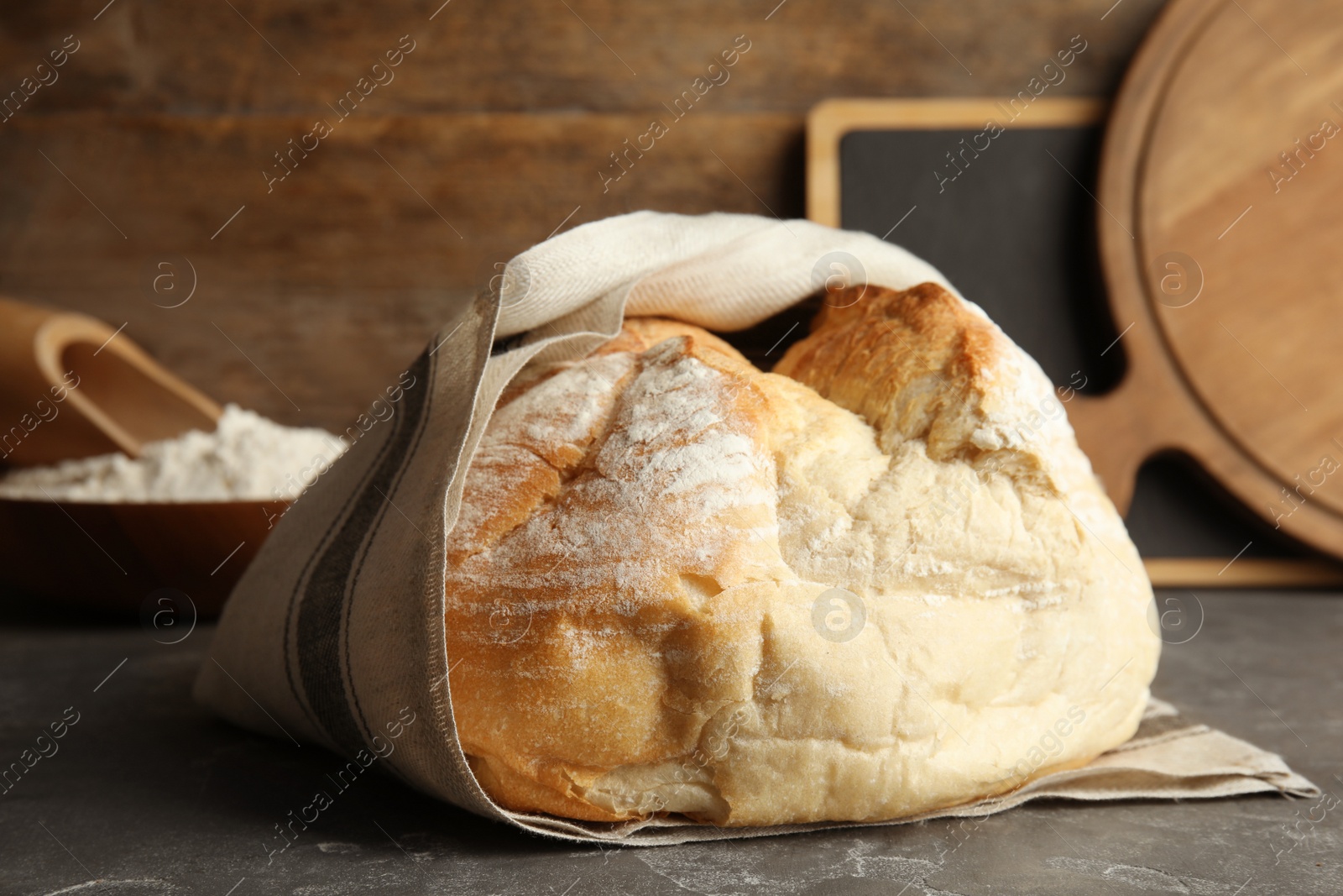 Photo of Loaf of fresh bread wrapped in fabric on grey table, closeup