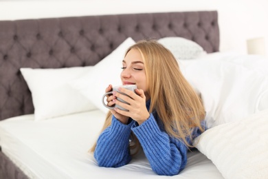 Beautiful young woman lying with cup in bed at home. Winter atmosphere