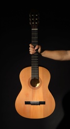 Man holding acoustic guitar on black background, closeup