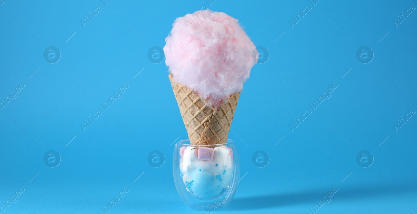 Photo of Sweet cotton candy in waffle cone on light blue background