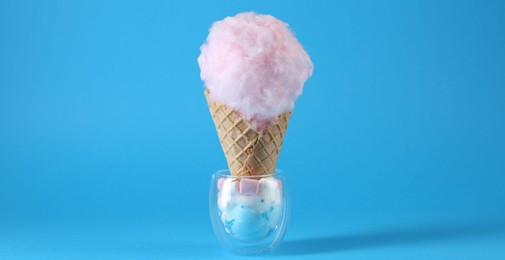 Photo of Sweet cotton candy in waffle cone on light blue background