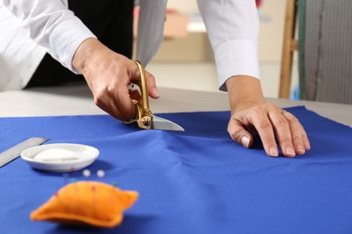 Photo of Seamstress cutting fabric at table in workshop, closeup