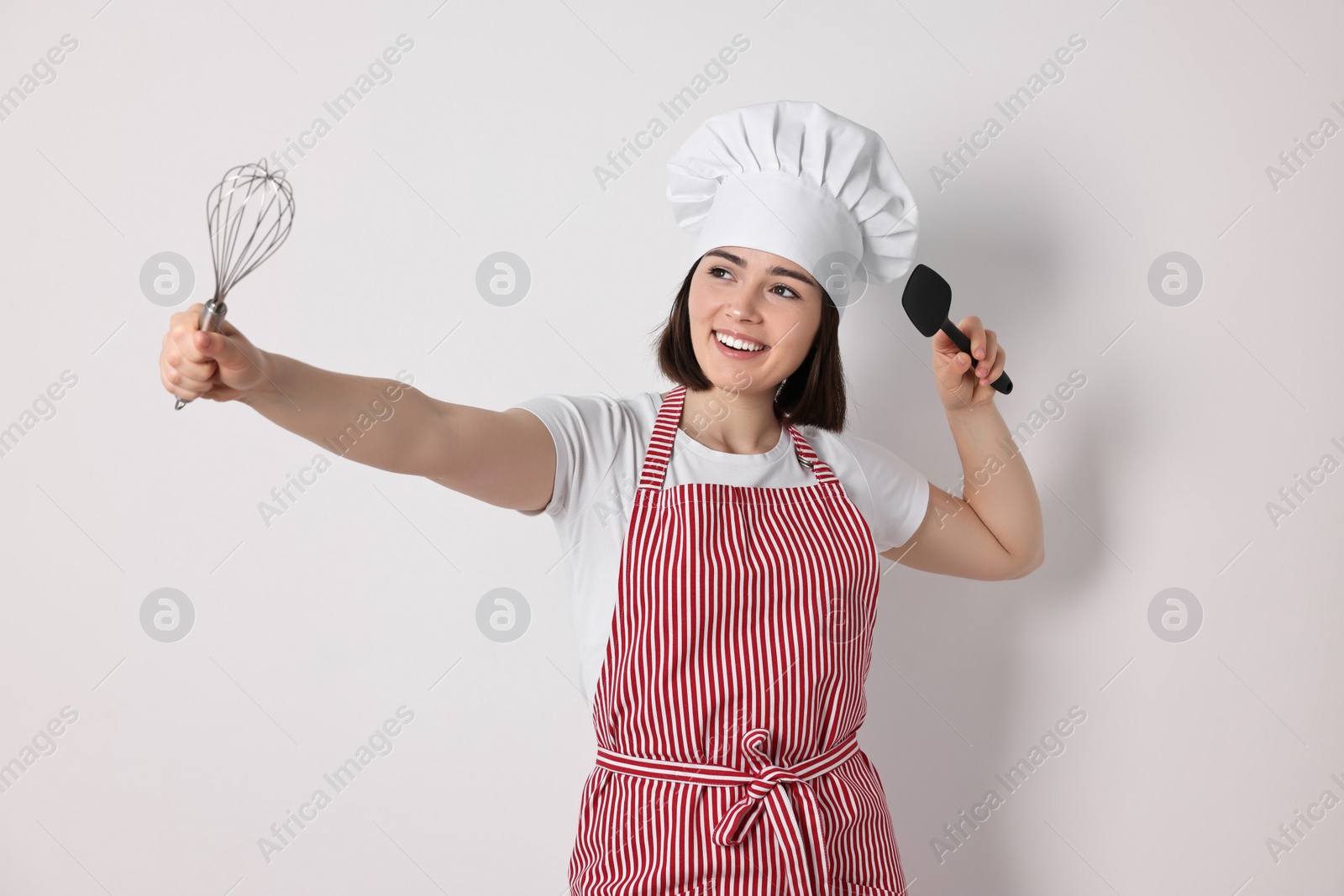 Photo of Happy confectioner with whisk and spatula on light grey background