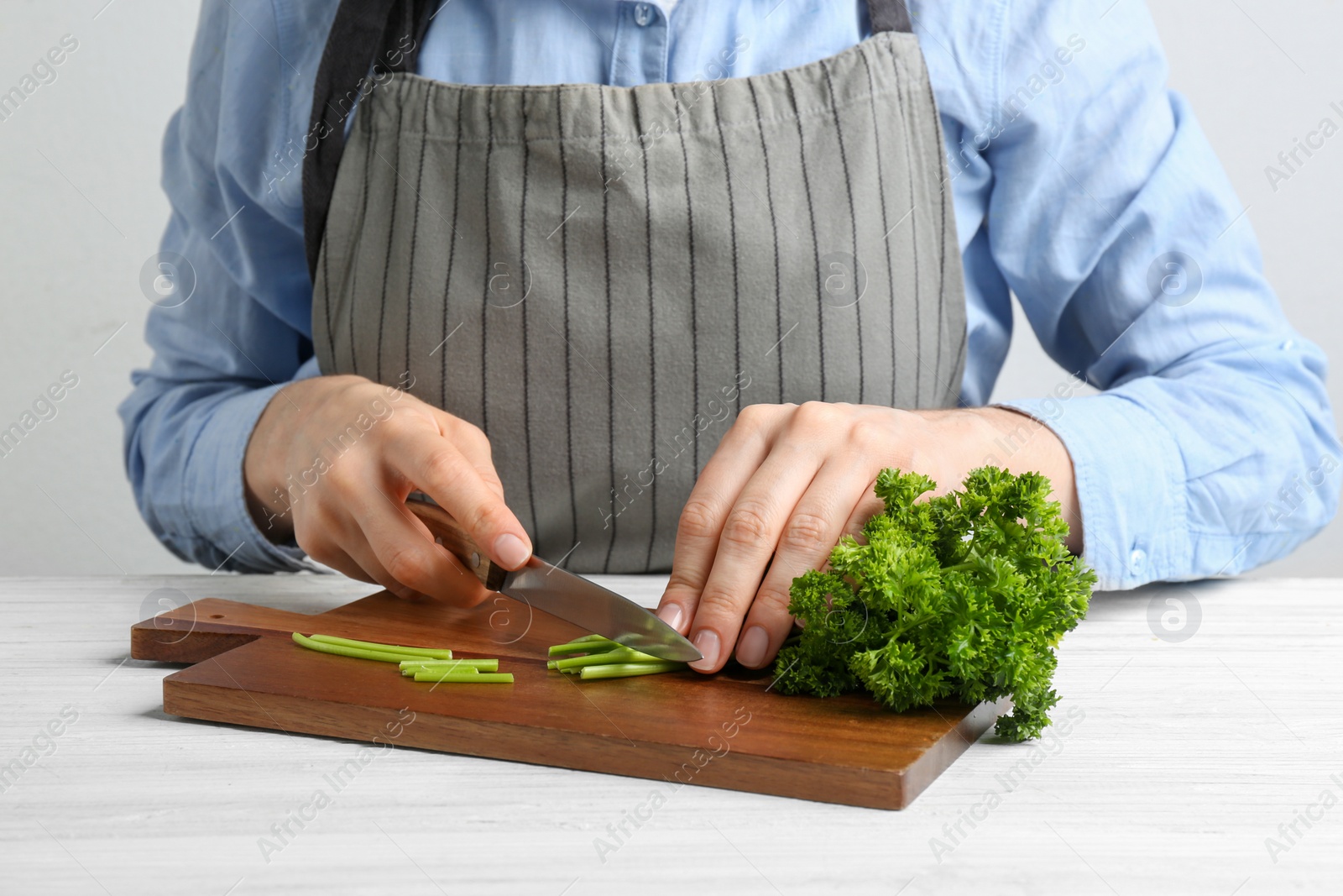 Photo of Woman cutting curly parsley at white wooden table, closeup