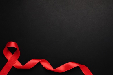 Photo of Top view of red ribbon on black background, space for text. AIDS disease awareness