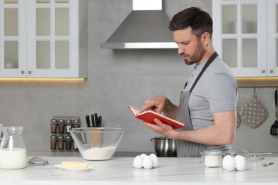 Photo of Man cooking by recipe book in kitchen