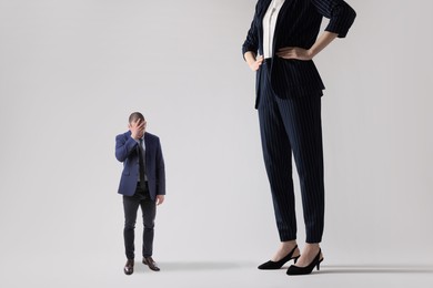 Giant woman and sad small man on light background