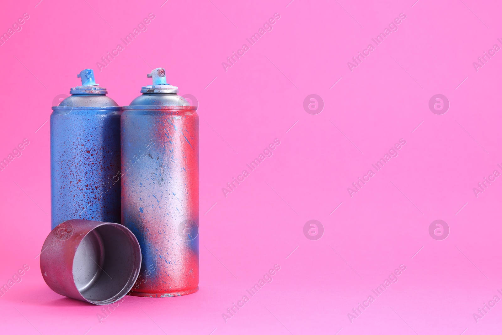 Photo of Spray paint cans with cap on pink background, space for text