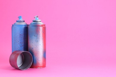 Photo of Spray paint cans with cap on pink background, space for text