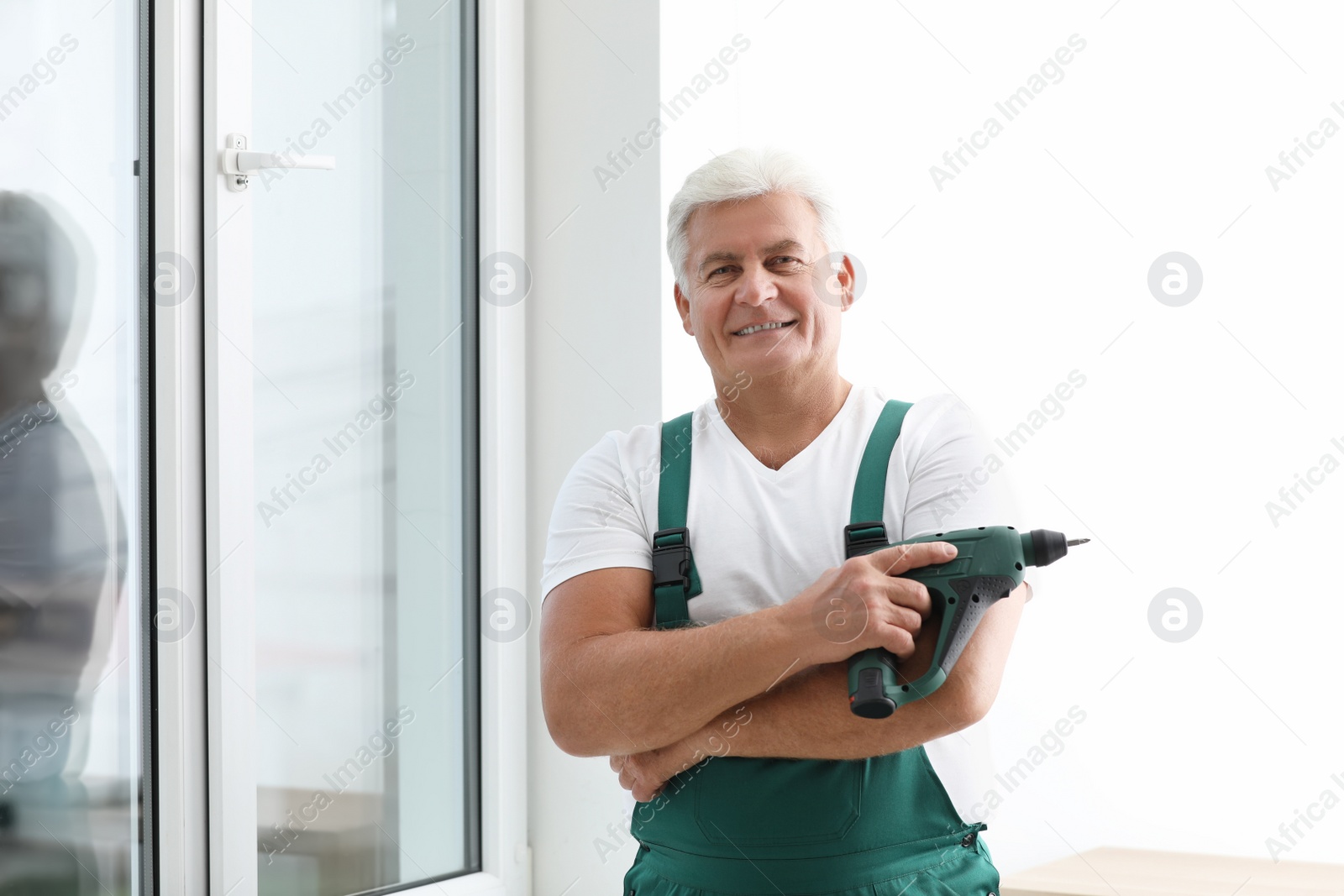 Photo of Mature repairman with electric screwdriver near plastic window indoors