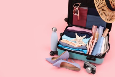 Photo of Open suitcase with clothes, beach accessories and shoes on pink background, space for text. Summer vacation