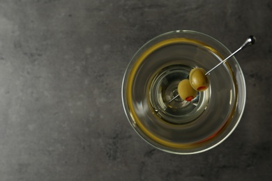 Photo of Glass of Classic Dry Martini with olives on grey table, top view. Space for text