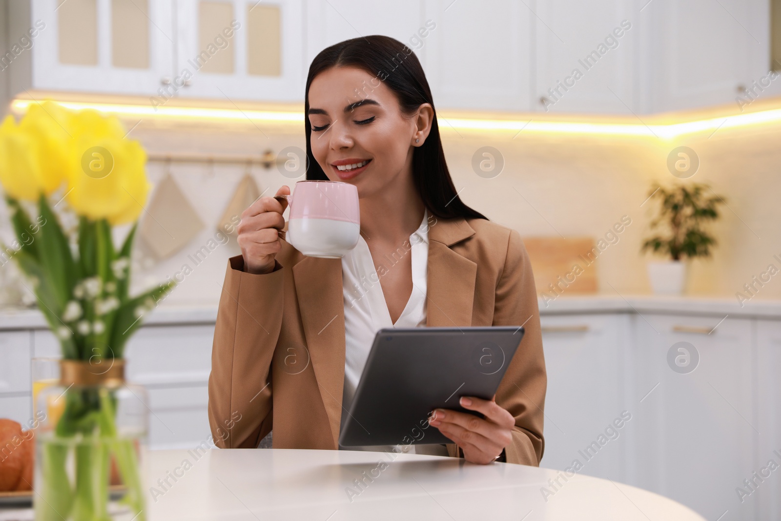 Photo of Young woman with tablet having breakfast in kitchen. Morning routine