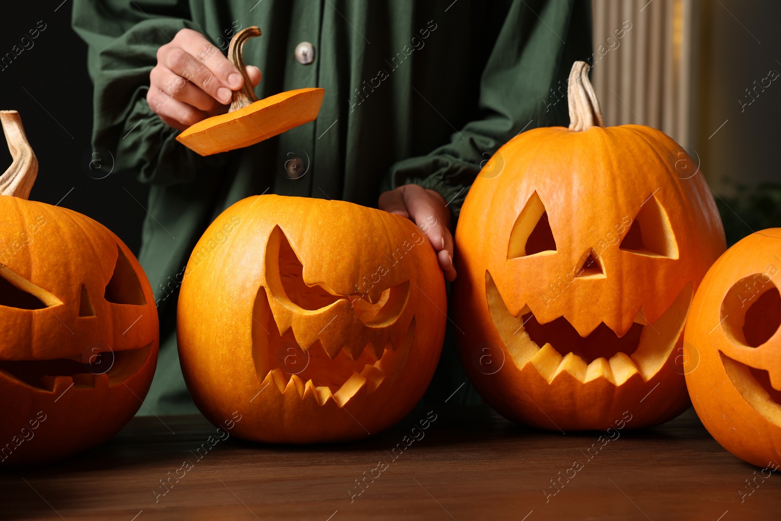 Photo of Woman with carved pumpkins for Halloween at wooden table, closeup