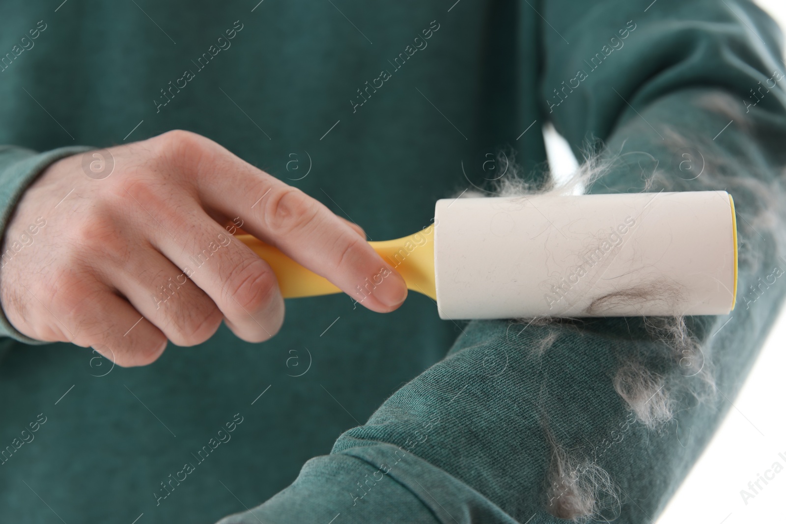 Photo of Man removing hair from green sweatshirt with lint roller on light background, closeup