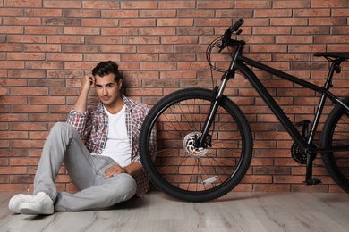 Photo of Handsome young man with modern bicycle near brick wall indoors