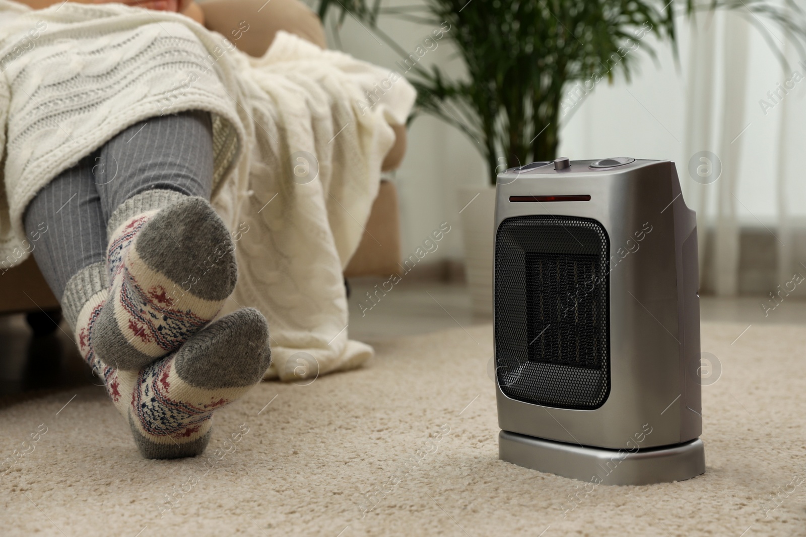 Photo of Woman warming legs near halogen heater at home, closeup