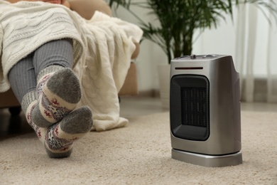 Photo of Woman warming legs near halogen heater at home, closeup