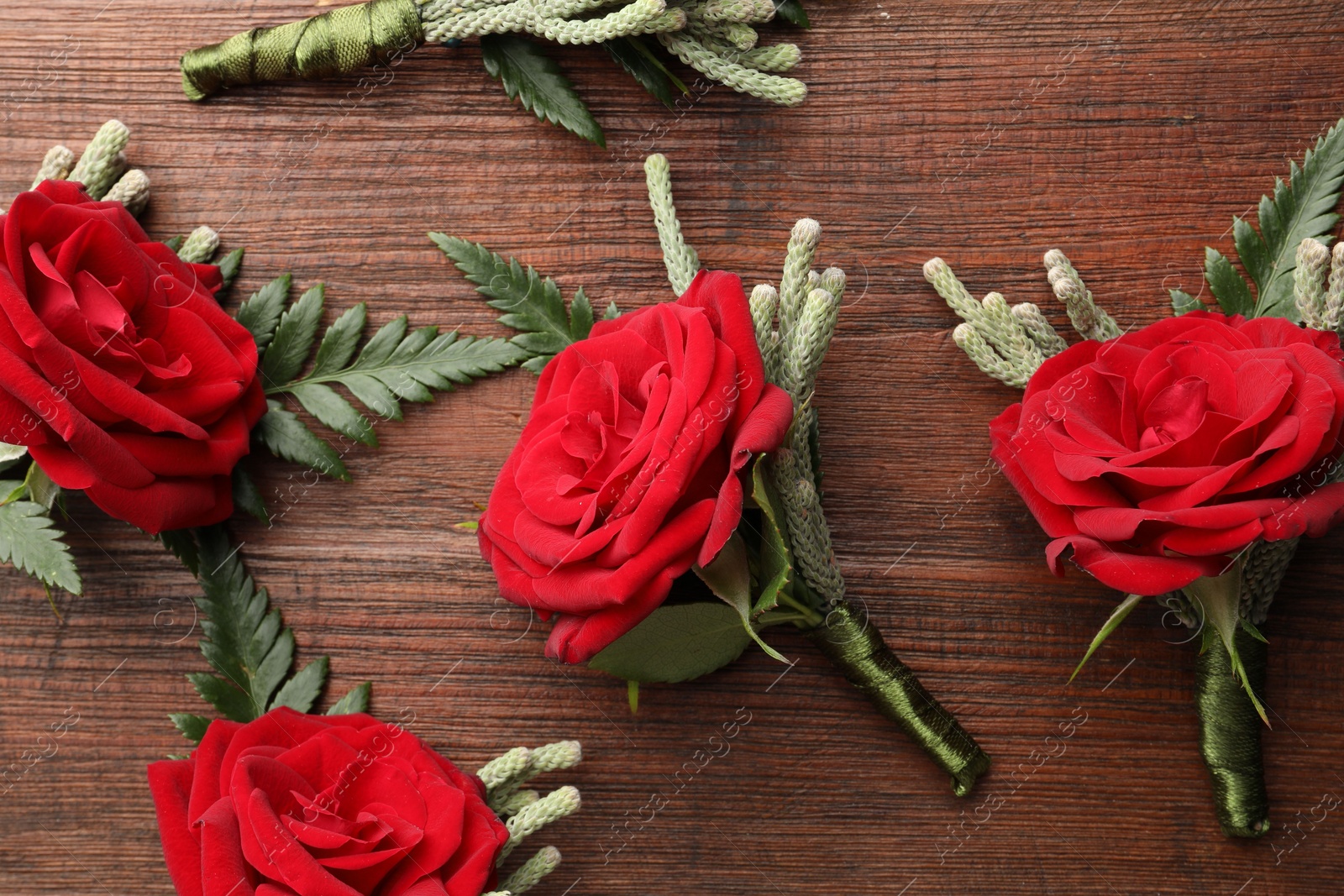 Photo of Many stylish red boutonnieres on wooden table, flat lay