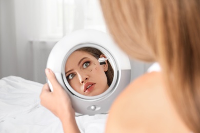 Photo of Young woman with eyelash loss problem looking in mirror indoors