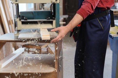 Working man using thickness planer at carpentry shop, closeup