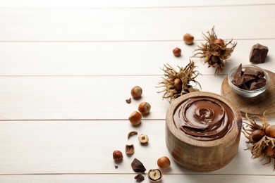 Bowl of tasty chocolate paste with hazelnuts on white wooden table, space for text