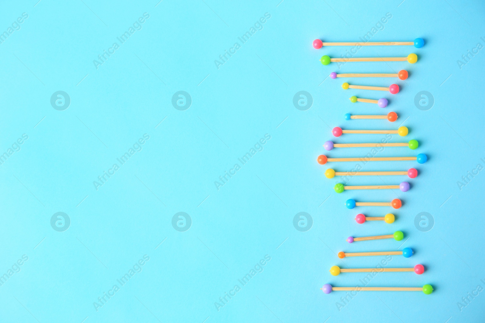 Photo of DNA molecule model made of toothpick and colorful beads on light blue background, flat lay. Space for text