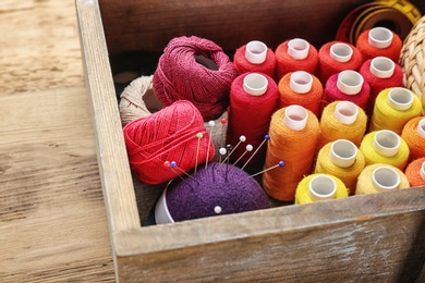 Box with color sewing threads on wooden background