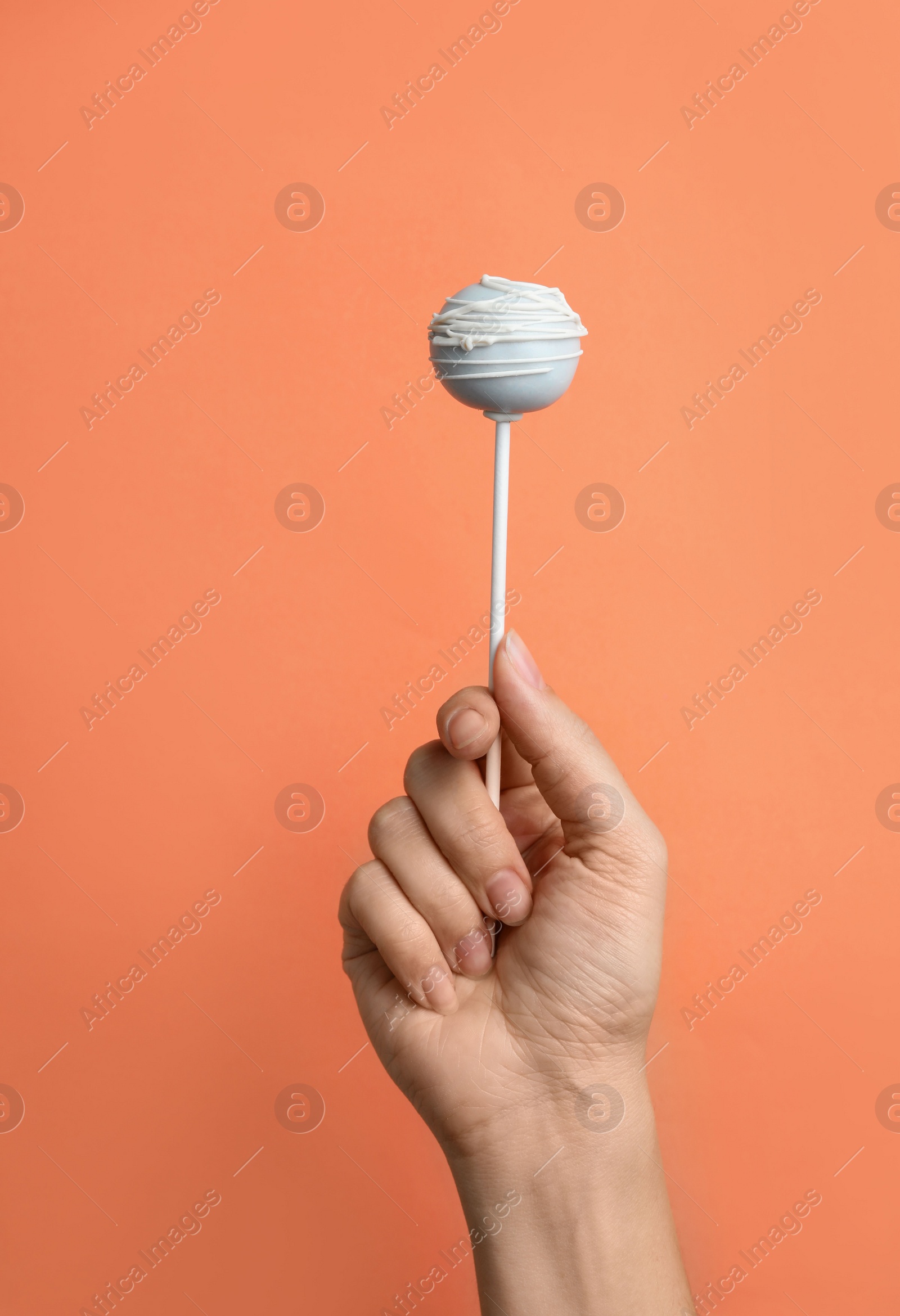 Photo of Woman holding sweet cake pop on coral background, closeup