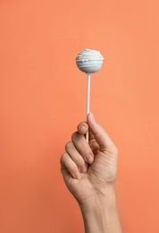 Photo of Woman holding sweet cake pop on coral background, closeup