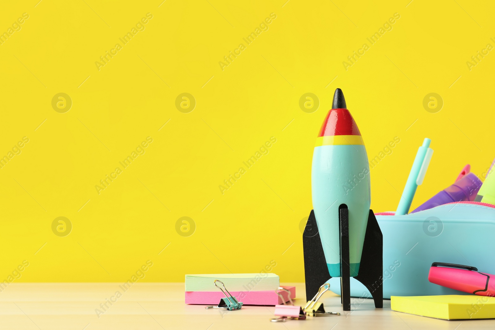 Photo of Bright toy rocket and school supplies on wooden table. Space for text