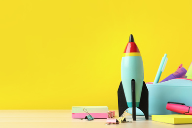 Photo of Bright toy rocket and school supplies on wooden table. Space for text