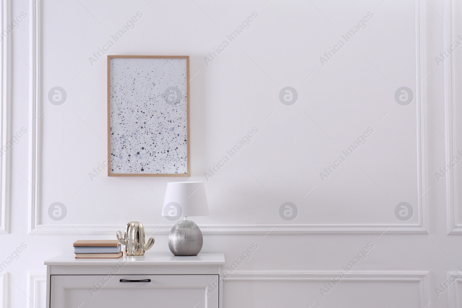 Photo of Wooden chest of drawers with books and lamp near white wall in room, space for text. Interior design